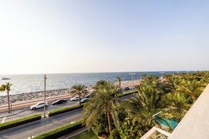 A coastal road with parked cars, palm trees, and a view of the sea.
