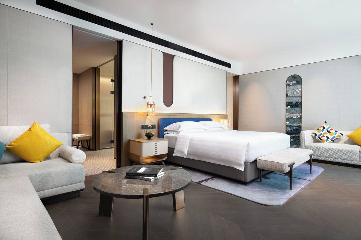 A modern hotel room with a bed, a sofa, a coffee table, and a nightstand.