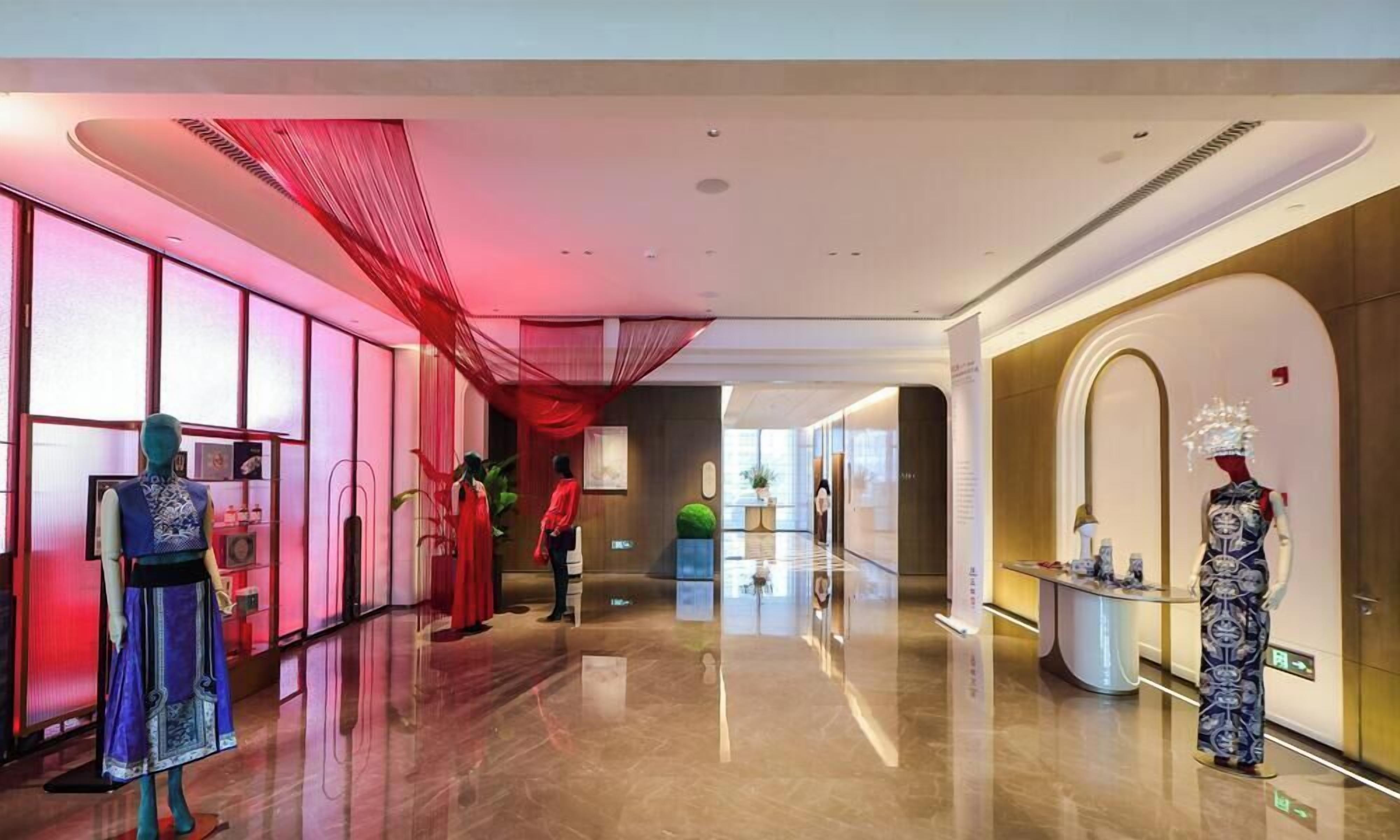 Un pasillo de hotel con maniquíes vestidos con atuendo formal, un techo cubierto con tela roja y un piso brillante.