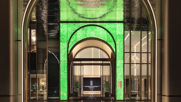 Ingresso moderno di un hotel con facciata illuminata di verde e pavimento riflettente.