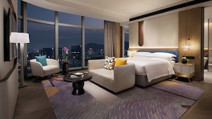 Una camera d'hotel moderna con un letto grande, un divano, un tavolino e vista sulla città illuminata di notte.