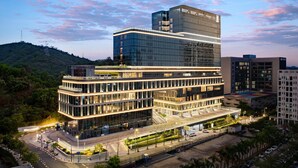 A modern multi-story building with a glass facade, surrounded by greenery and a hilly landscape. - MGallery Shenzhen (Shenzhen)