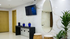 A modern lobby with a marble wall, a flat-screen TV, a large mirror, a console table with decorative vases, two wooden stools, and potted plants. - Ibis Styles Foz Do Iguaçu (Foz do Iguaçu)