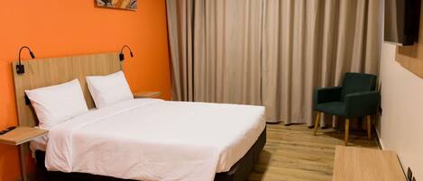 A hotel room with a bed, a desk, a chair, a TV, and a painting on the wall.