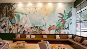A modern lounge area with a large mural of tropical wildlife, comfortable seating, and a large window providing a view of the street. - Ibis Styles Foz Do Iguaçu (Foz do Iguaçu)