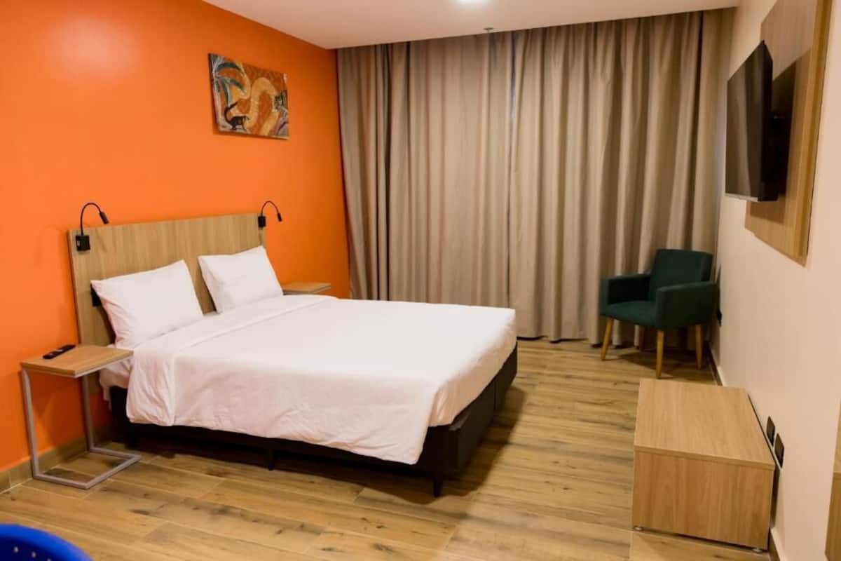 Ein Hotelzimmer mit Bett, Schreibtisch, Stuhl und einem an der Wand befestigten Fernseher.
