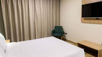 A hotel room with a bed, a chair, a TV, and a wooden bench.
