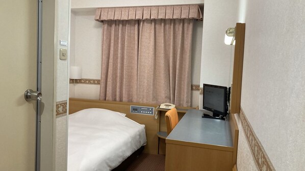 Una habitación de hotel con una cama, un escritorio con una computadora, un teléfono y una ventana con cortinas.