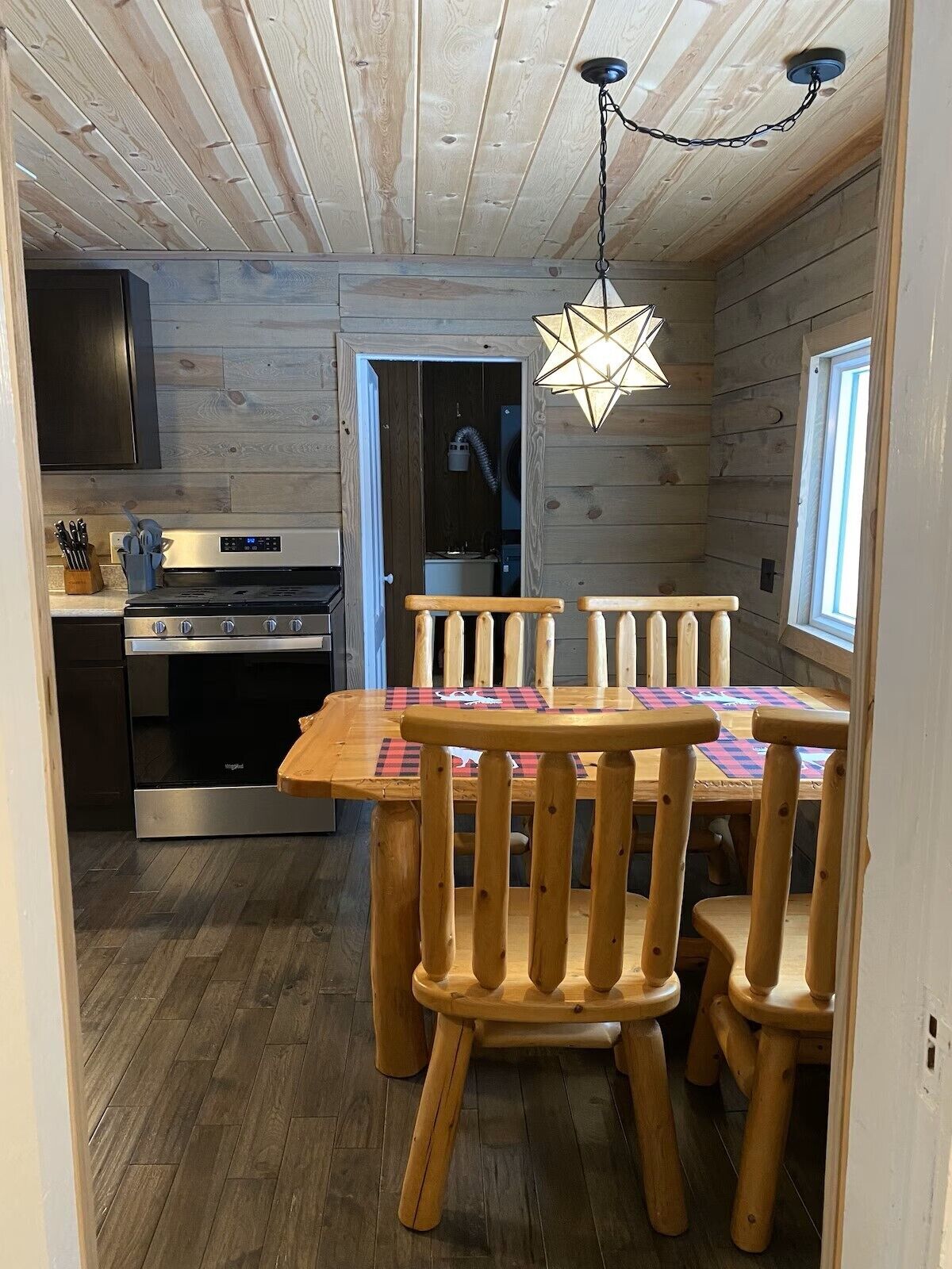 A wooden interior with a dining table and chairs, a kitchen with a stove and oven, and a ceiling light fixture.