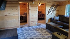 A cozy cabin interior with a wooden floor, a sofa, a bed, and a ceiling fan. - Amazing Lake Superior view from Ridge Road w/2 car heated garage, pet friendly (Grand Marais)