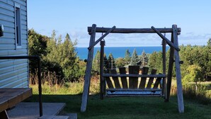 A wooden swing set in a grassy area with a view of the ocean. - Amazing Lake Superior view from Ridge Road w/2 car heated garage, pet friendly (Grand Marais)