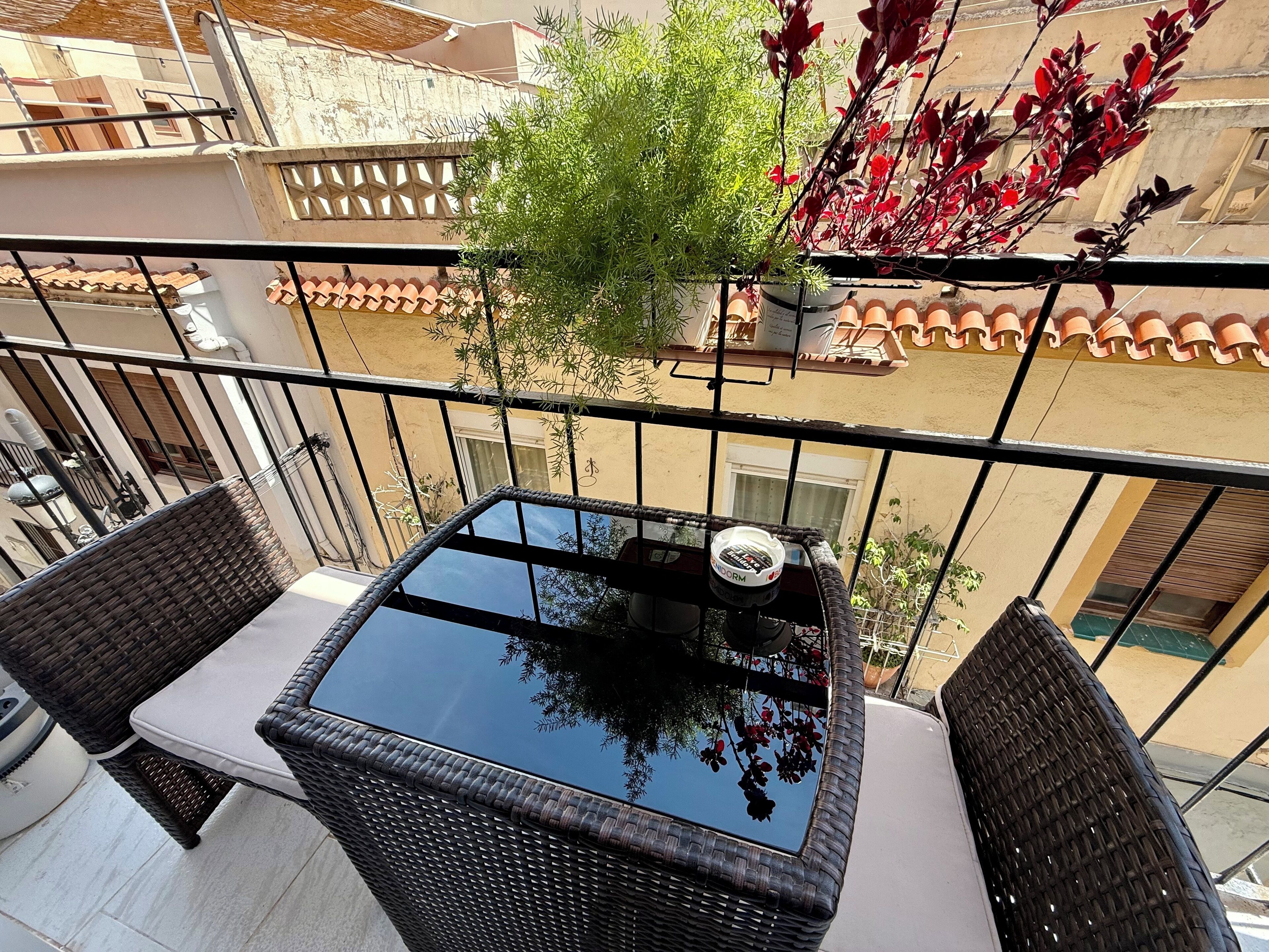 A balcony with wicker furniture, a glass table, and a potted plant.