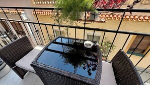 Un balcón con mobiliario de mimbre, una mesa de vidrio y una planta en maceta.