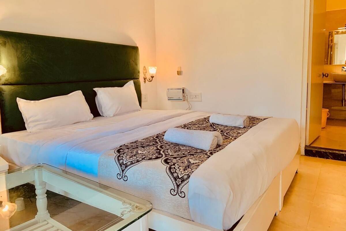A double bed with white linens, a patterned throw blanket, and a bedside table with a lamp.