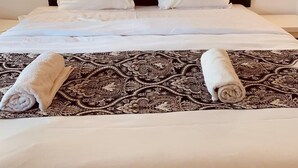 Un lit bien fait, avec une couvre-lit à motifs, deux serviettes enroulées et une tête de lit rembourrée de couleur vert foncé.