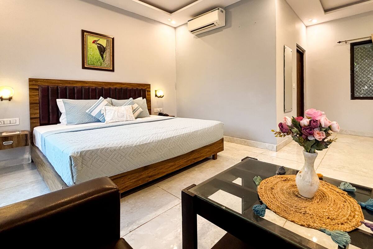 A hotel room with a bed, bedside table, and a vase of flowers.