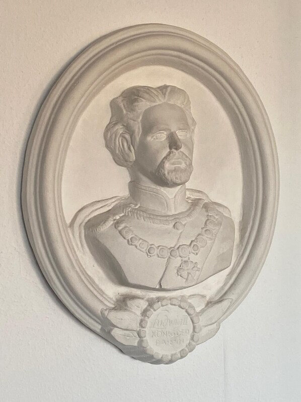 Una escultura de busto con un marco decorativo, que presenta un collarado detallado y una medalla con texto.