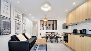A modern kitchen with wooden cabinets, a dining area with a black table and chairs, and a black sofa with white cushions. - Super appartment-2BR/6p-Bastille (Paris)