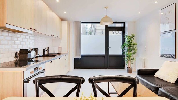 A modern kitchen with a dining area, featuring a black and white color scheme, a dining table with two chairs, and a black sofa with a white cushion. - Super appartment-2BR/6p-Bastille (Paris)