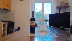 A kitchen with a wine bottle on the counter, a TV, and a window with a view of trees.