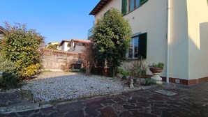 A courtyard with a gravel path, a tree, and a building with a balcony.