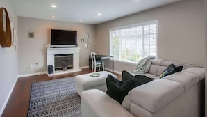 A living room with a fireplace, a sofa, a TV, and a window with blinds.