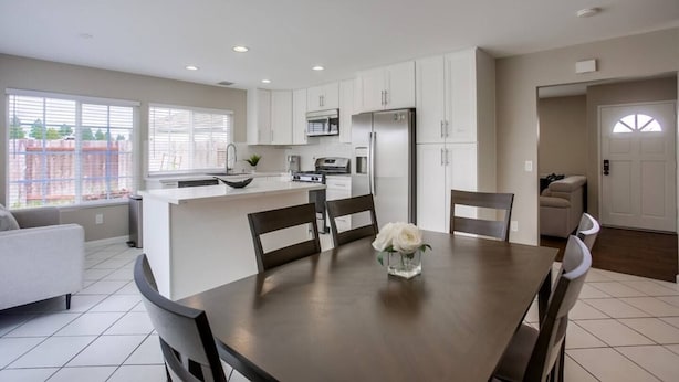 A modern kitchen with white cabinets, a central island, and a dining area with a table and chairs.