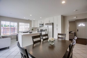 A modern kitchen with white cabinets, a central island, and a dining area with a table and chairs. - 15 Min to La Jolla Shores Beach and Torrey Pines! (San Diego)