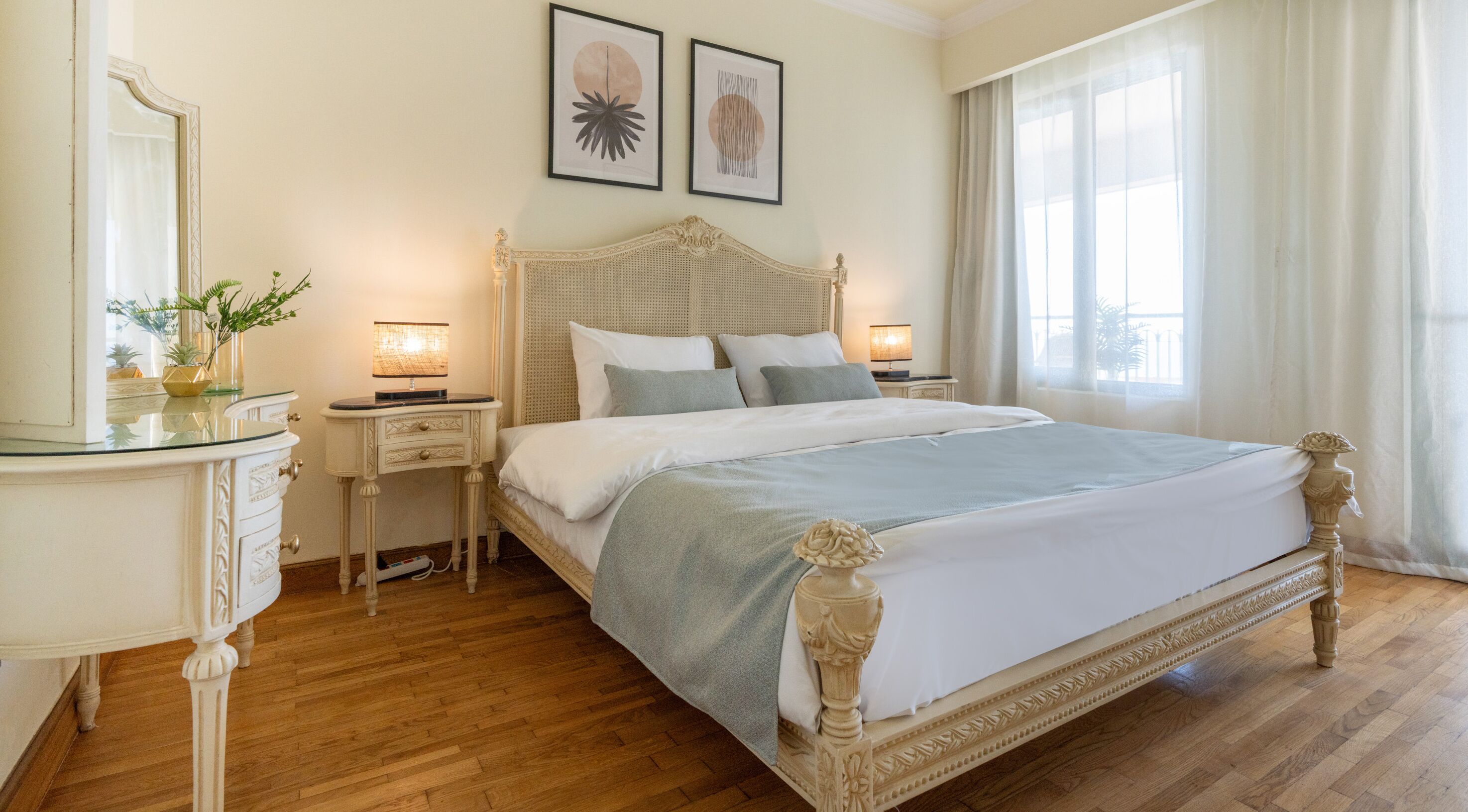 A spacious bedroom with a large bed, two bedside tables, a nightstand, a dresser, and a mirror.