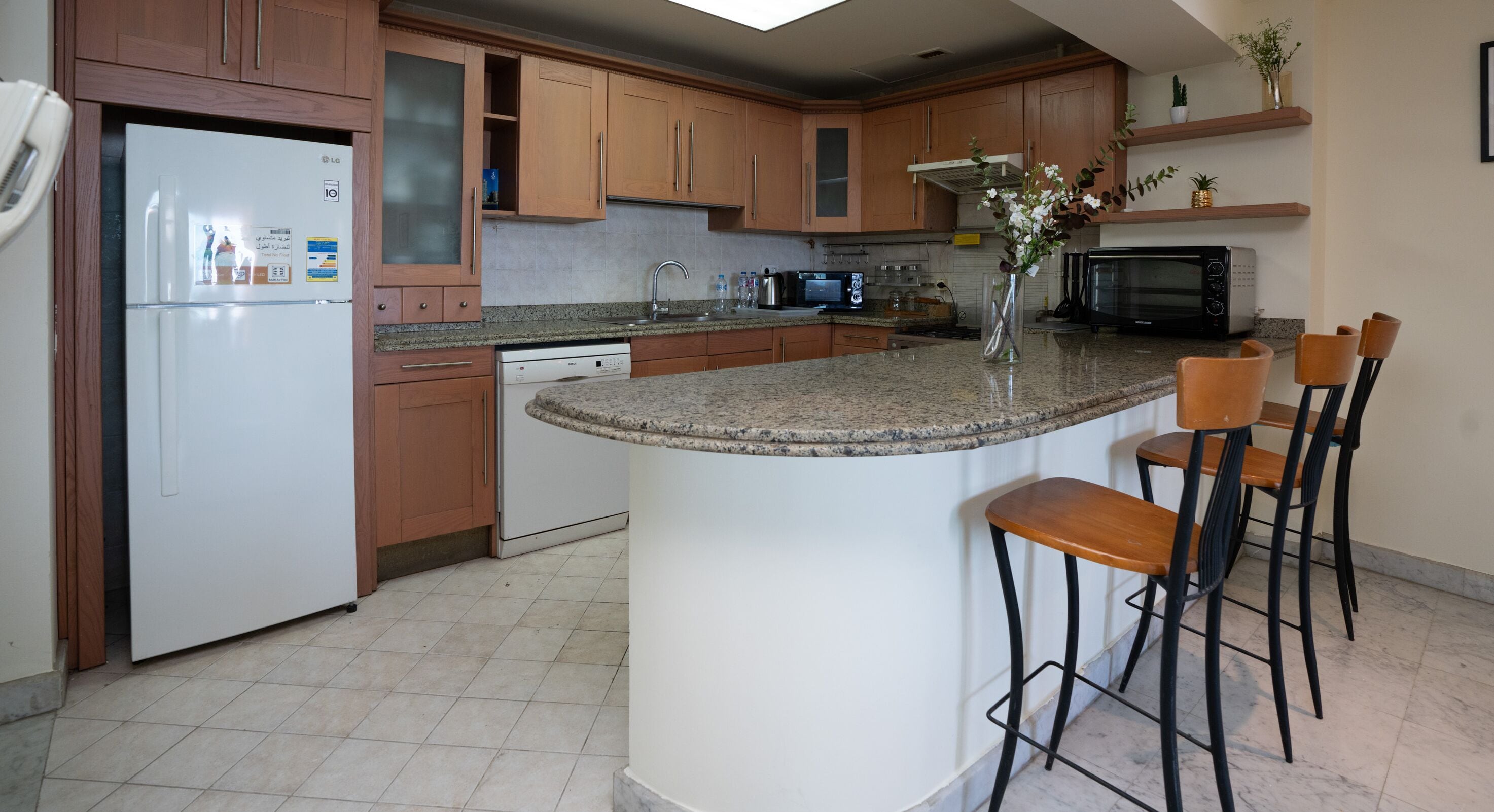 Una cocina con armarios de madera, un refrigerador blanco, lavavajillas integrado, encimera de granito, microondas y una pequeña isla con taburetes de bar.