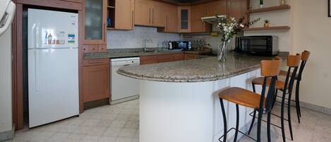 Una cocina con armarios de madera, un refrigerador blanco, lavavajillas integrado, encimera de granito, microondas y una pequeña isla con taburetes de bar.