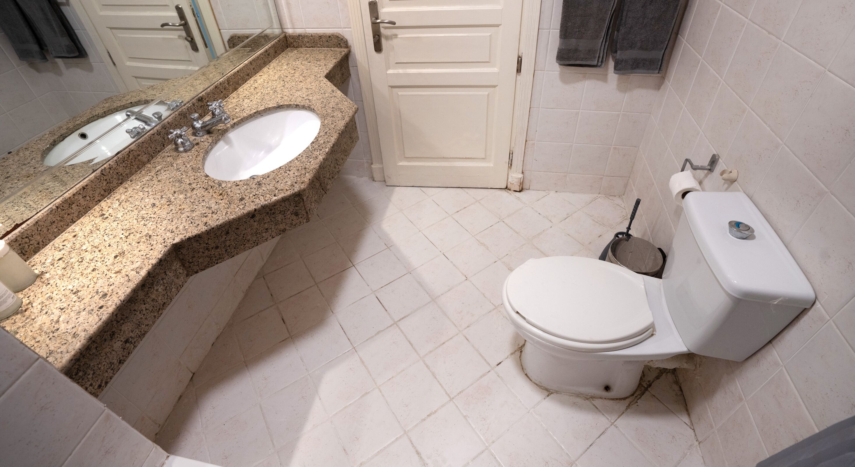A bathroom with a granite countertop, a white sink, a toilet, and a shower area.