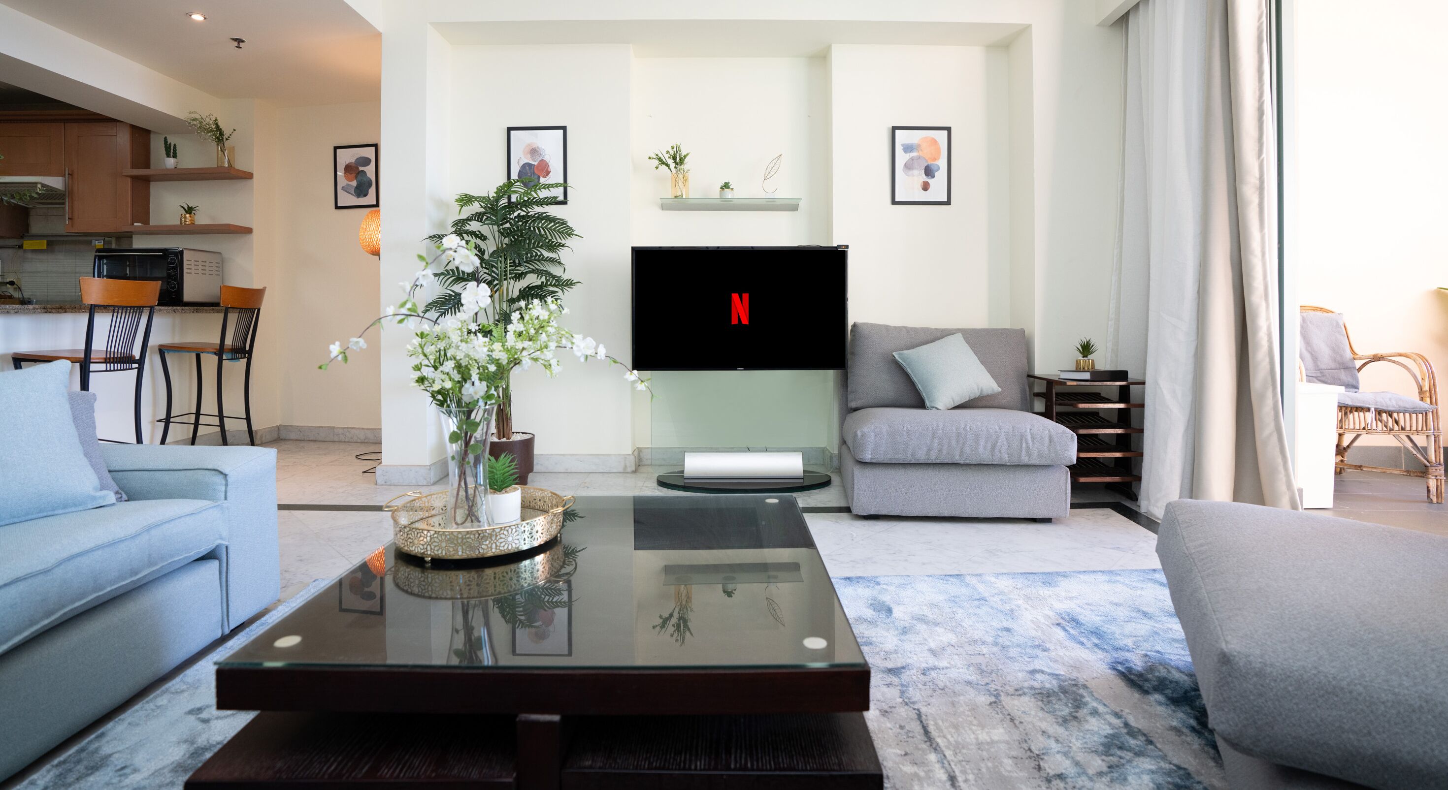 Een moderne woonkamer met een flatscreen televisie, een salontafel met een bloevas, een grijze bank en een blauwe fauteuil.