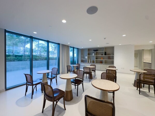A modern dining area with round tables and wicker chairs, large windows, and a white interior.