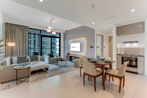 A modern living room with a sofa, coffee table, and dining area with chairs. There is a kitchen with a stove and cabinets. - Coastal Chic 1 Bedroom Apartment w private beach (Dubai)