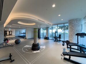 A gym with exercise equipment, a punching bag, and a large pillar with numbers. - Coastal Chic 1 Bedroom Apartment w private beach (Dubai)