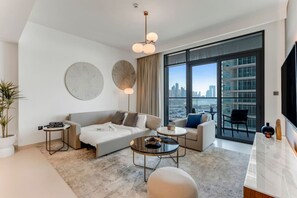 A modern living room with a sofa, two armchairs, a coffee table, and a TV. There are large windows with a city view.
