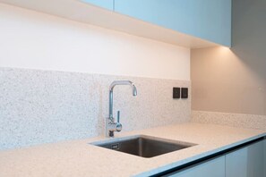 A modern kitchen with a stainless steel sink, a single faucet, and a light-colored countertop. - Coastal Chic 1 Bedroom Apartment w private beach (Dubai)