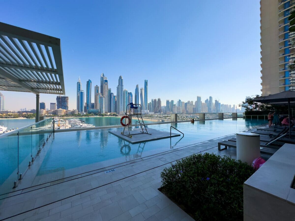 A rooftop infinity pool with a city skyline view, lounge chairs, and a lifebuoy.