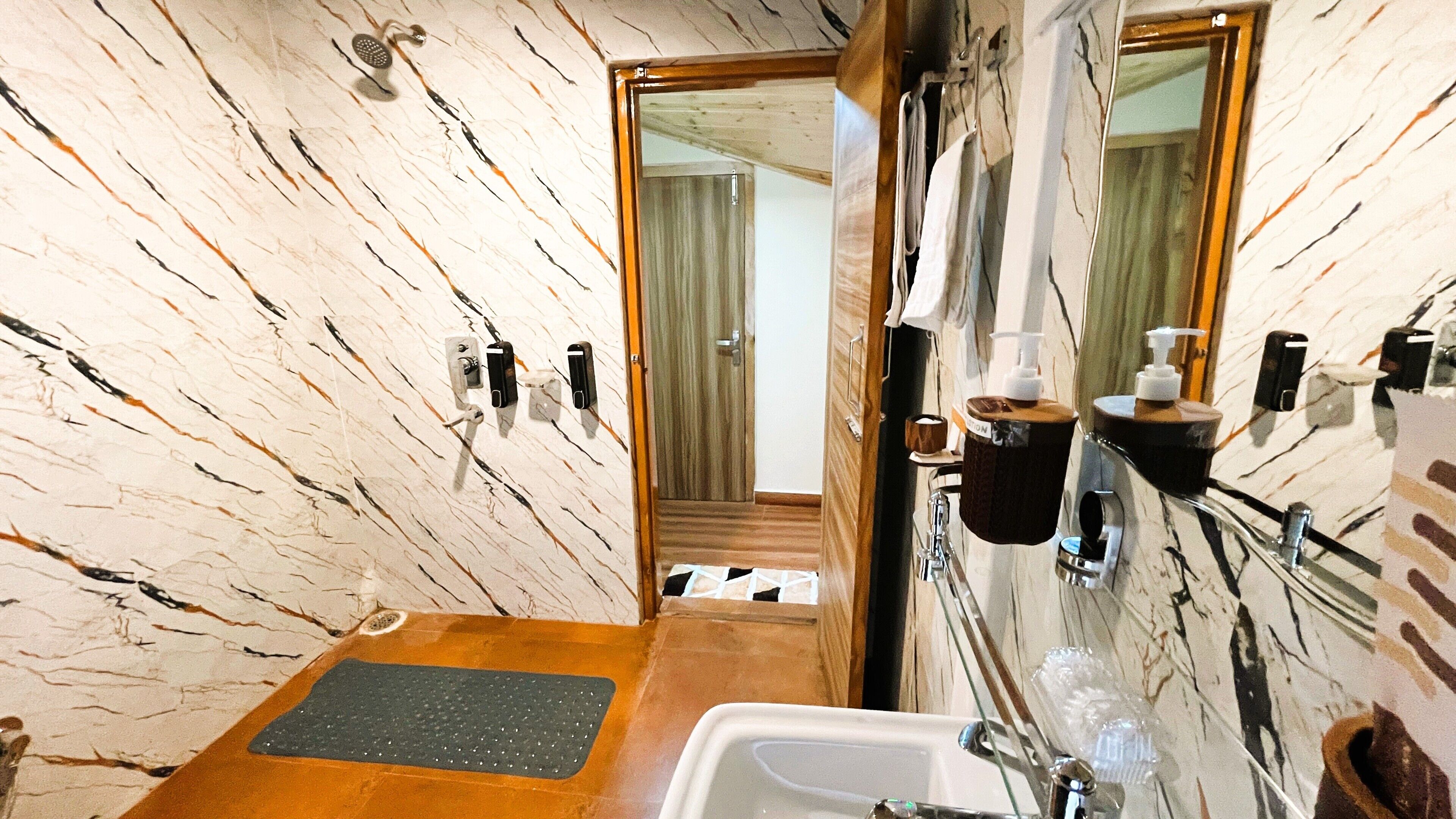 A bathroom with a marble wall, a sink, a mirror, and a shower.