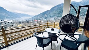 A balcony with a table and chairs, a hanging chair, and a view of a mountainous landscape. - Wander Thrives Inn By Ads (Manali)