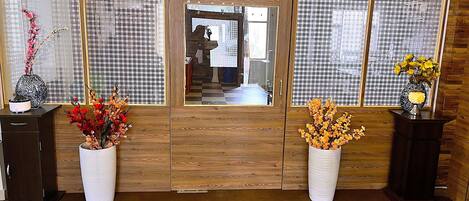 A room with a wooden door, a checkered floor, and two vases with flowers on pedestals.