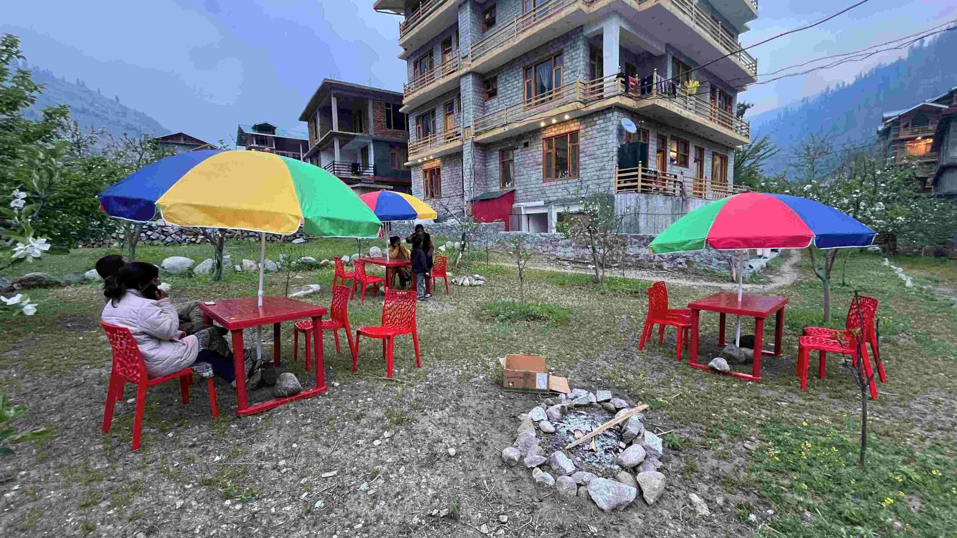 Outdoor seating with umbrellas, a stone building, and a mountainous backdrop.