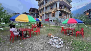 Outdoor seating with umbrellas, a stone building, and a mountainous backdrop.