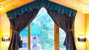 A room with a large window, curtains, and a view of a building outside. - Wander Thrives Inn By Ads (Manali)