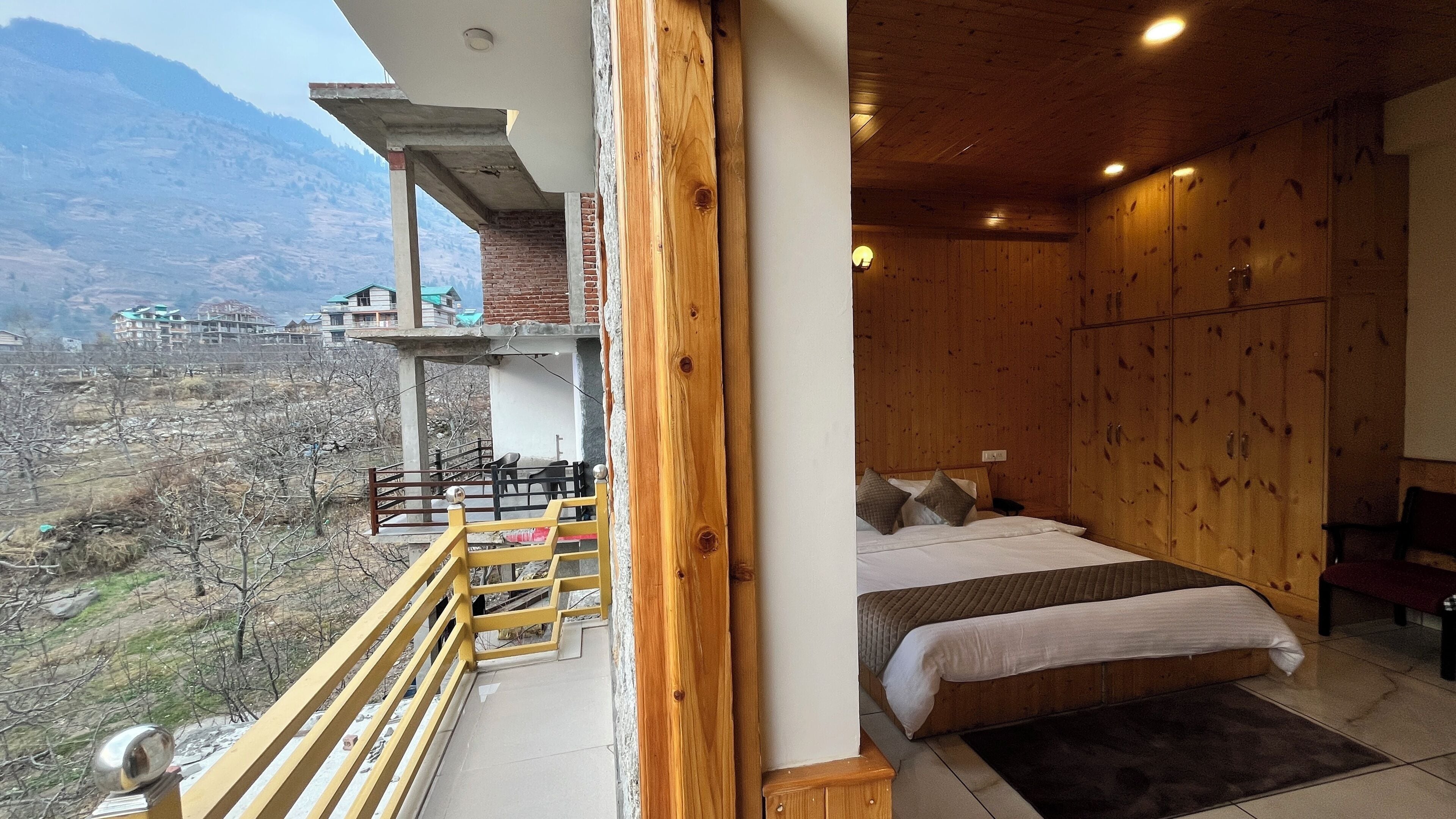 A bedroom with a wooden bed, a balcony with a railing, and a view of a mountainous landscape.