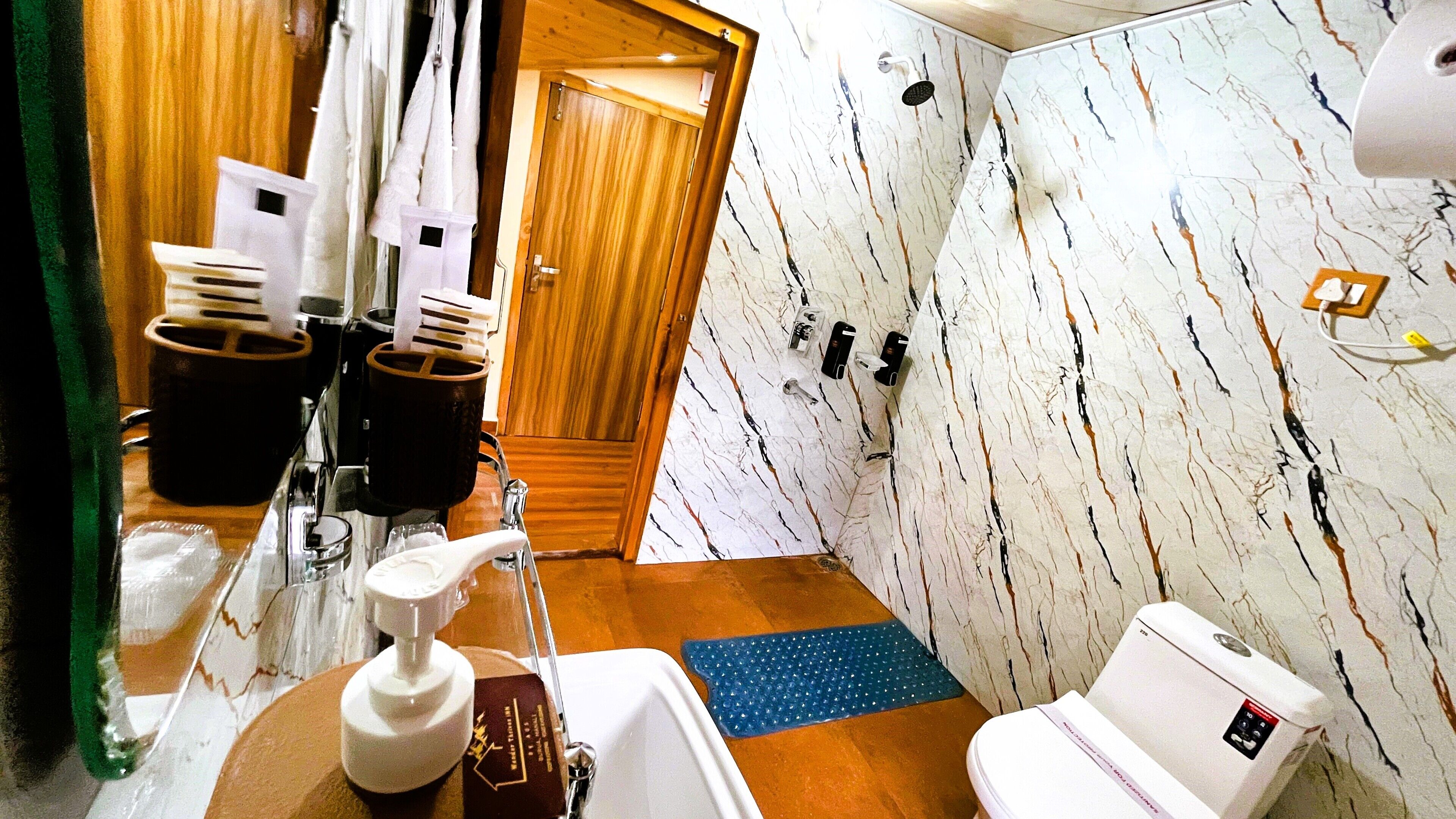 A bathroom with a marble wall, a sink, a toilet, and a shower area.