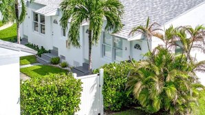 A white two-story house with a tiled roof, surrounded by lush greenery and palm trees. - Sunset Cove In Hollywood FL, FREE Parking (Hollywood)