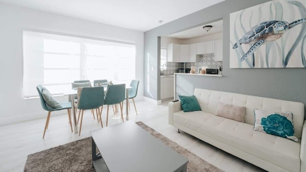 A modern living room with a white sofa, teal chairs, and a dining area with a table and chairs. - Sunset Cove In Hollywood FL, FREE Parking (Hollywood)