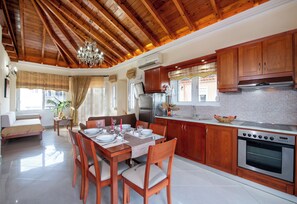 Een ruime keuken met houten kastjes, een eethoek met een tafel voor vier personen, en een zithoek met een bank en een raam.